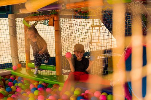 Portrait of two funny little kids playing in ball pit and enjoying time in childrens entertainment and play area, copy space