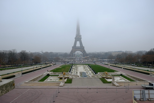 Paris, France - January the 25th 2023: The Eiffel tower lost in the fog, and the Varsow fountain in winter.