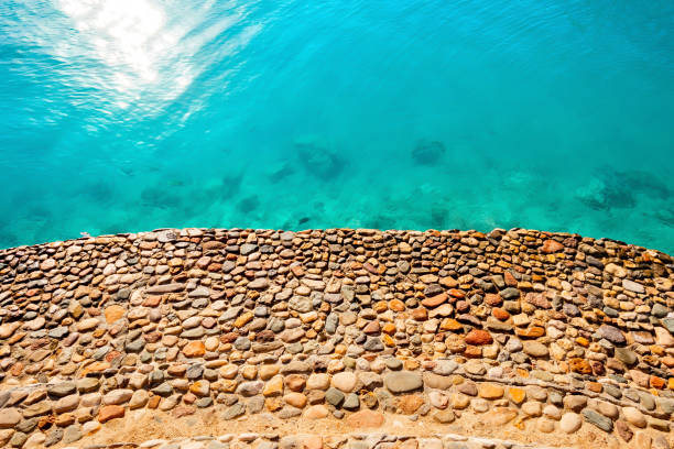 The shore is made of stone with blue clear water. Background.
