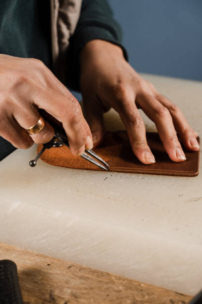 istock Process of creation genuine leather product. Craftsman is cutting genuine leather using cutter knife for creation natural leather products. Equipment for genuine leather production in workshop. 1459438290