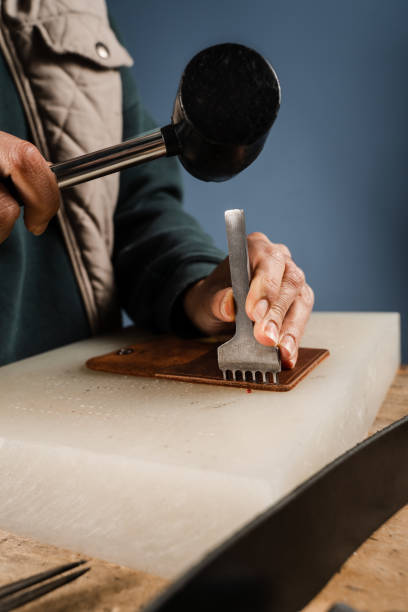 istock Craftsman is punching genuine leather using line punch and hammer for creation natural leather products. Tools of craftsman for belts creation. Equipment for genuine leather production in workshop. 1459438309