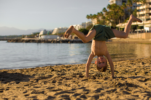 Little boy doing a handstand on the beach.Summer recreation and sports.