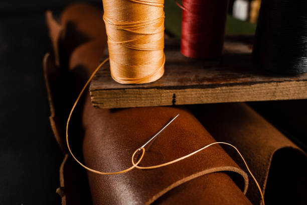 Close-up thread with needle on roll of brown genuine leather in craftsman workshop. Handmade genuine leather production in the factory. Close-up thread with needle on roll of brown genuine leather in craftsman workshop. Handmade genuine leather production in the factory sewing thread rolled up creation stock pictures, royalty-free photos & images