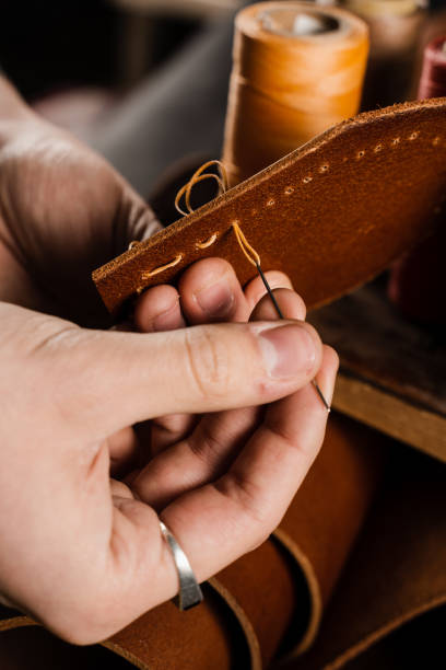 Process of stitching genuine leather. Craftsman sews genuine leather using needle and thread for creation natural leather products. Equipment for genuine leather production in workshop.