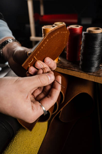 istock Craftsman sews genuine leather using needle and thread for creation natural leather products. Equipment for genuine leather production in workshop. Process of stitching genuine leather. 1459438728