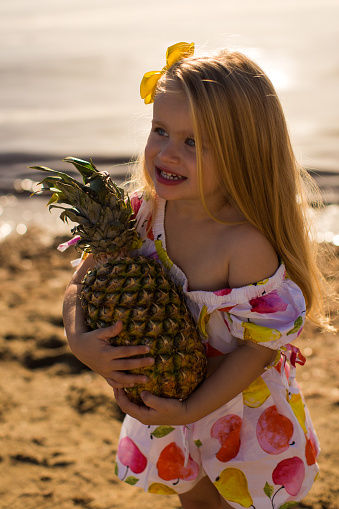 close up little girl with pineapple near the sea summertime