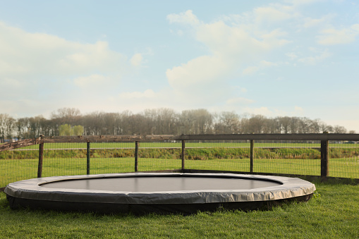 Big trampoline near wooden fence on green lawn outdoors