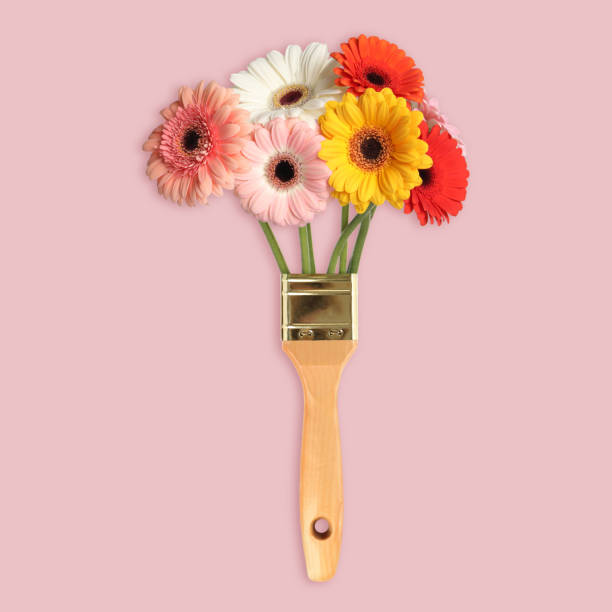 istock Creative design with paint brush and beautiful gerbera flowers on pink background. Spring is coming 1459443614