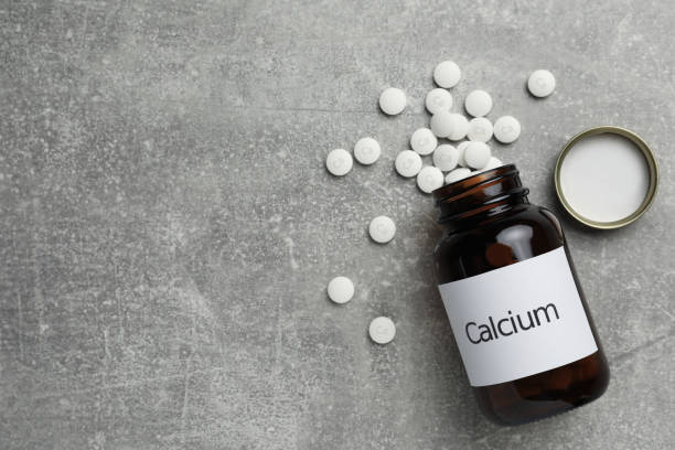 istock Overturned bottle of calcium supplement pills on grey table, flat lay. Space for text 1459444146