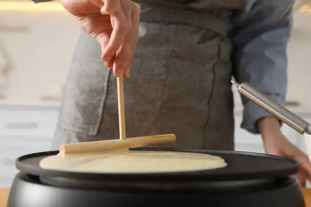 Woman cooking delicious crepe on electrical pancake maker in kitchen, closeup