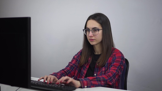 IT Specialist works for a PC. A young woman in glasses and a shirt is typing on a computer in the office. 4k