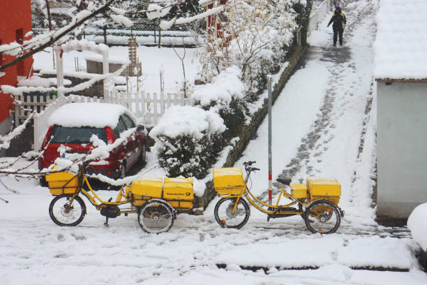 elektro-lastenräder der deutschen post parkten an einem kalten, verschneiten wintertag auf dem bürgersteig. - messenger deutsche post ag package germany stock-fotos und bilder