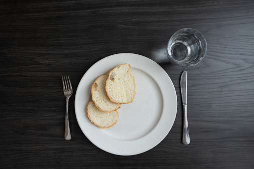 White plate with three slices of bread with a knife and fork and a glass of water on a dark wood table with copy space shot from above