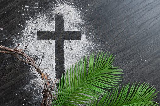 Christian lent background with cross of ashes, palm fronds and partial crown of thorns on a dark wood background with copy space