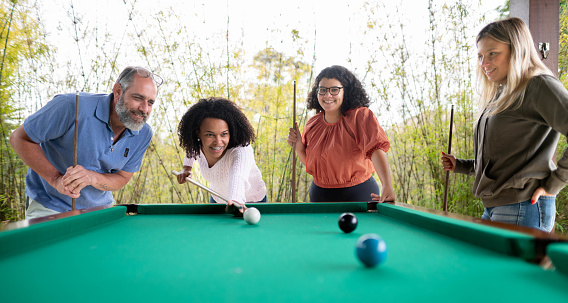 Smiling group of young female friends playing a game of pool with a parent outside on a patio