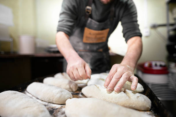 Baker scoring loaves of bread before baking them in an oven