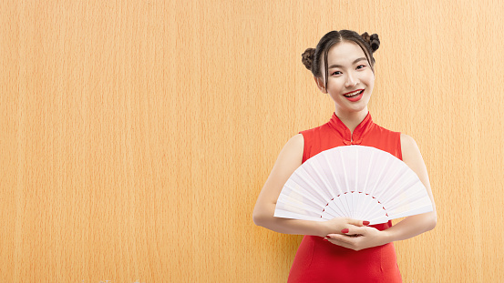 Asian Chinese woman in a cheongsam dress holding fan celebrates Chinese New Year. Happy Chinese New Year