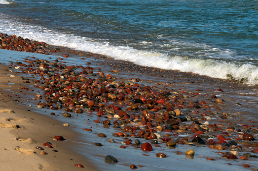 Colorful sea pebbles on the shore of the Baltic Sea on the background of an incoming wave, Curonian spit, Kaliningrad region, Russia