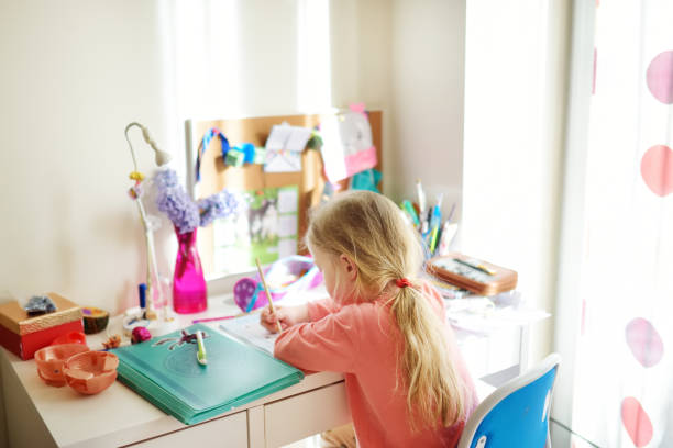 istock Smart little schoolgirl doing her homework at her table at home. Child learning to write and read. 1459500804