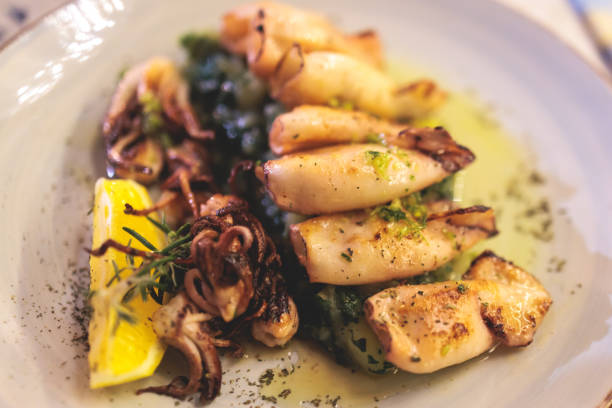 Fried grilled baby squids on a plate with garlic, lemon and mashed potato garnish served in a traditional seafood restaurant in Montenegro, prepared cooked calamari on the table