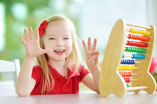 Cute little girl playing with wooden abacus at home. Smart child learning to count. Preschooler having fun with educational toy at home or kindergarten.