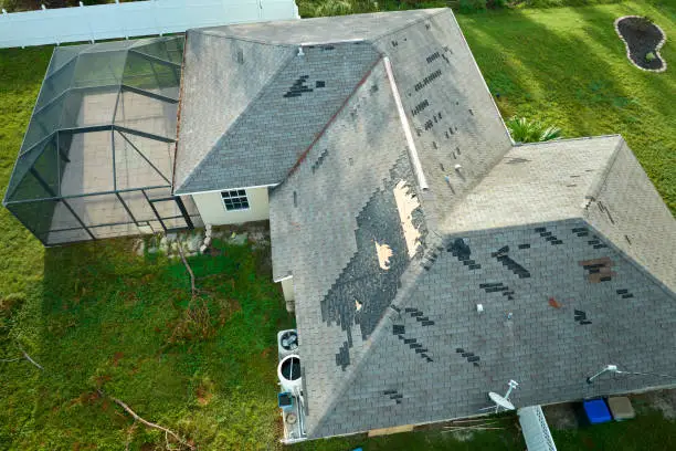 Photo of Wind damaged house roof with missing asphalt shingles after hurricane Ian in Florida. Repair of home rooftop concept