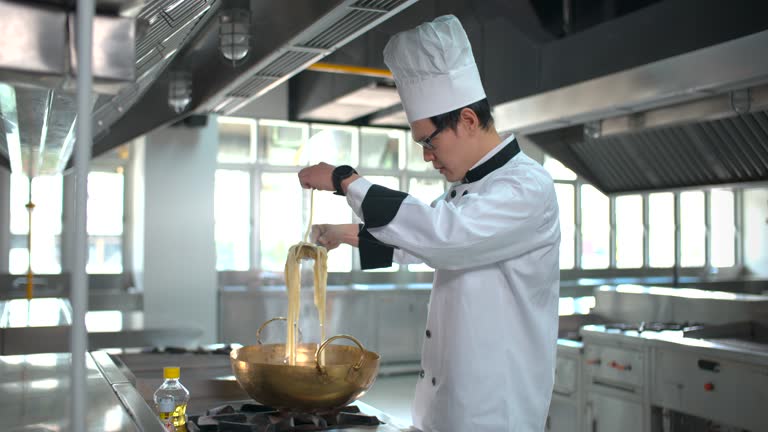 Male chef in white uniform cooking spaghetti in industrial kitchen.