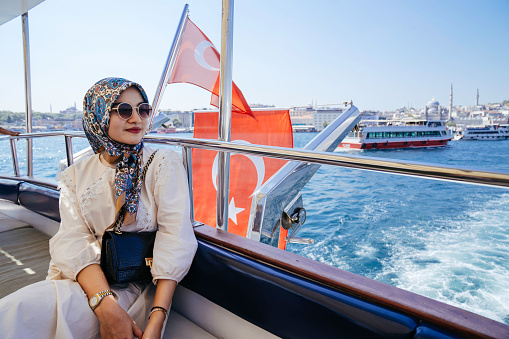 a young muslim traveler lady smiling while leaning side of a boat