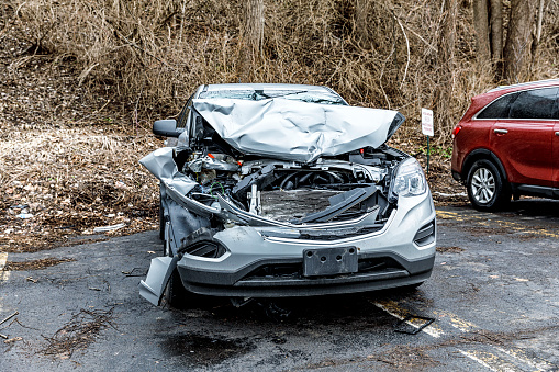 Front end view of a very heavily damaged, crumpled and totaled wrecked junkyard car awaiting complete disassembly to be recycled as spare / replacement parts. Car parked in a salvage yard parking lot in Fairport, New York, near Rochester - January 9, 2019.