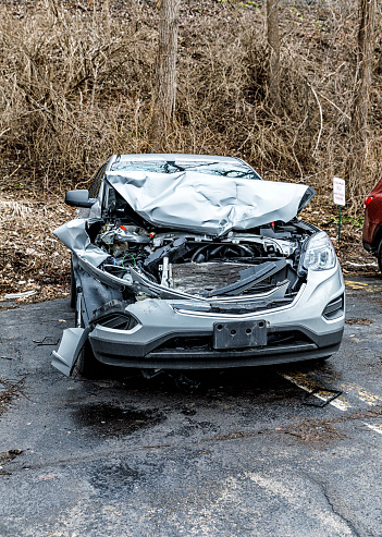 Front end view of a very heavily damaged, crumpled and completely totaled car wreck awaiting disassembly to be recycled as spare / replacement parts. Car parked at a salvage junkyard in Fairport, New York, near Rochester - January 9, 2019.