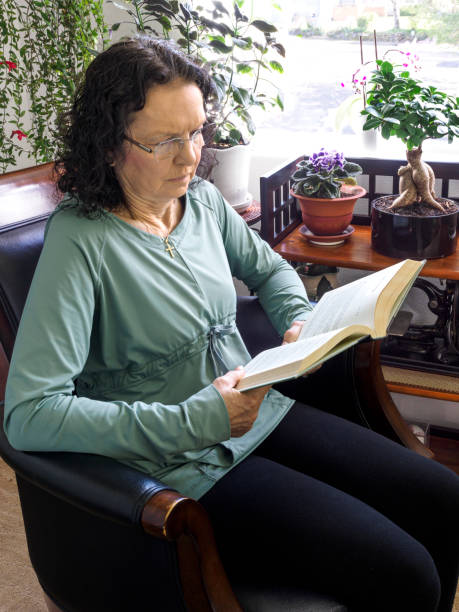 istock Senior Woman Reading a Book by Plants and Window 1459510918