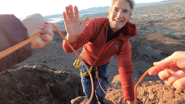 First person view from hands of belayer to mature man climbing