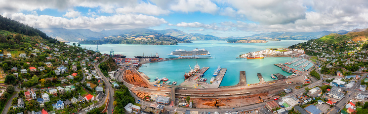 Scenic panorama of Diamond harbour in Lyttleton port town of New zealand with busy cargo terminal and passenger cruise ship at wharf.
