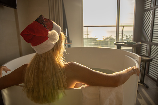 Young woman takes a bath in hotel room, she wears a Santa hat