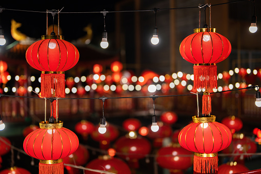 Many red Chinese New Year lanterns are hung and there are light bulbs decorated beside them, very beautiful, and there is a bokeh in the background at night