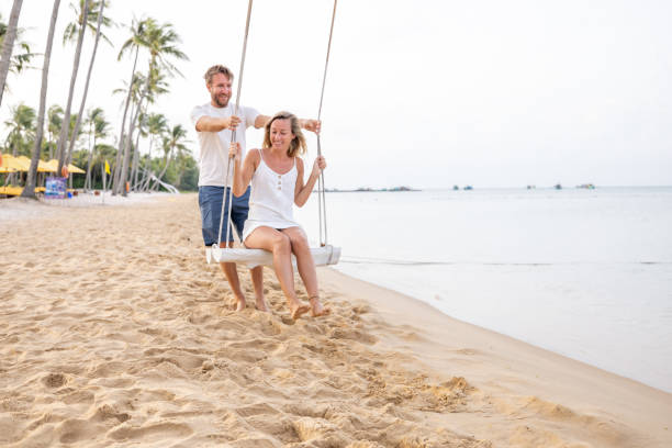 istock Playful young couple on tropical beach using swings at sunrise 1459519229