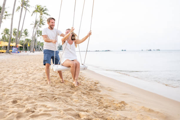 istock Playful young couple on tropical beach using swings at sunrise 1459519230