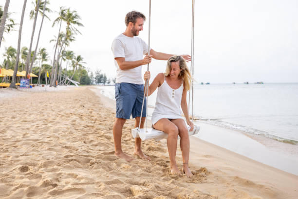 istock Playful young couple on tropical beach using swings at sunrise 1459519396