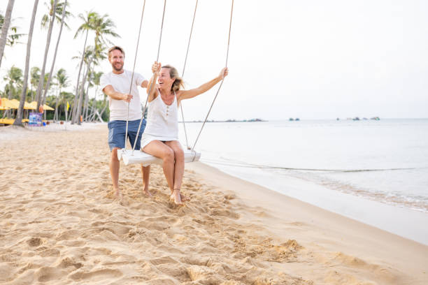 istock Playful young couple on tropical beach using swings at sunrise 1459519448