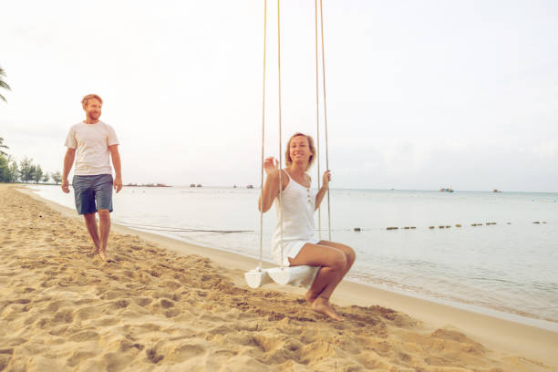 istock Playful young couple on tropical beach using swings at sunrise 1459519530