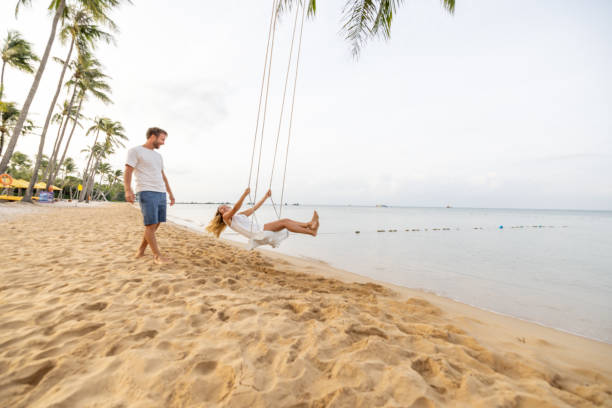 istock Playful young couple on tropical beach using swings at sunrise 1459519583