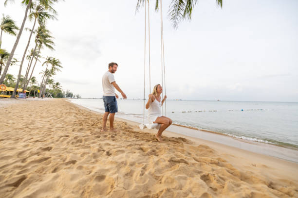 istock Playful young couple on tropical beach using swings at sunrise 1459519594