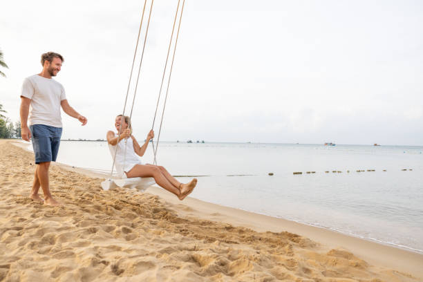 istock Playful young couple on tropical beach using swings at sunrise 1459519635