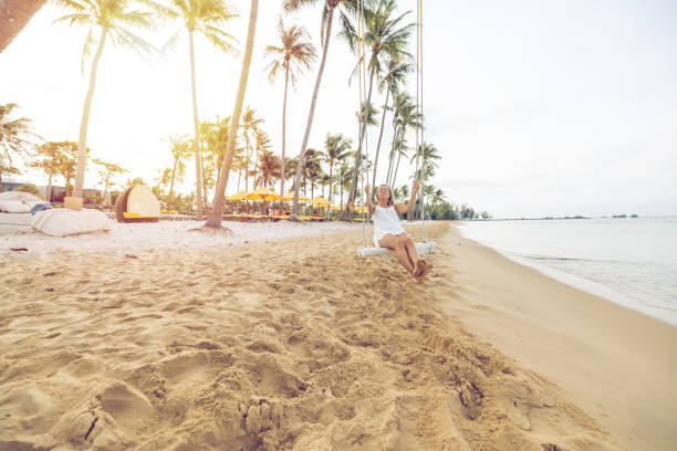 istock Playful young woman on tropical beach using swing at sunrise 1459520181