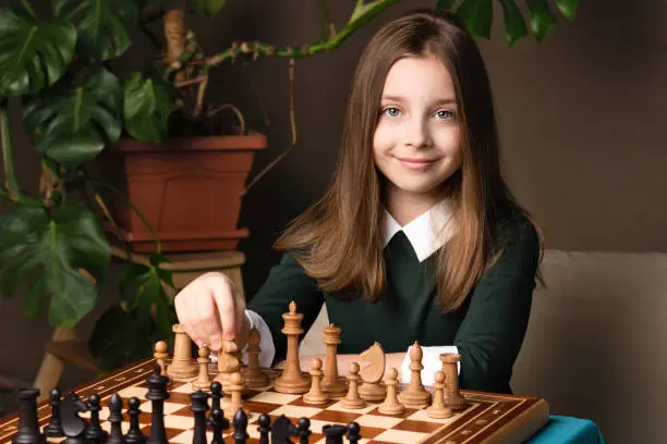 Schoolgirl chess player plays game with white pieces. Female teen sitting at chessboard. Young girl playing chess.