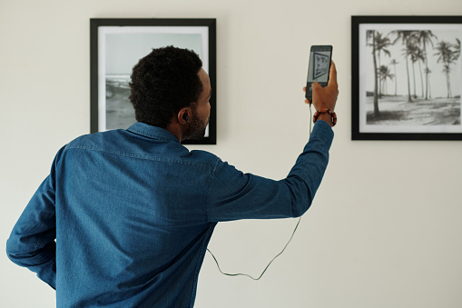 Man scanning qr code on photograph in art gallery to listen to auidioguide