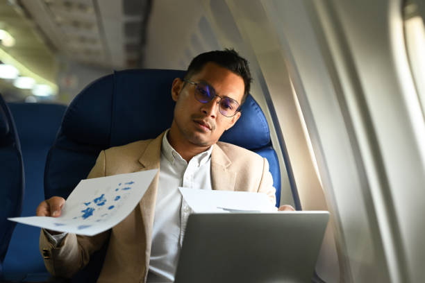 istock Stressed businessman working with financial document while sitting on airplane cabin. Business or travel abroad concept. 1459547297