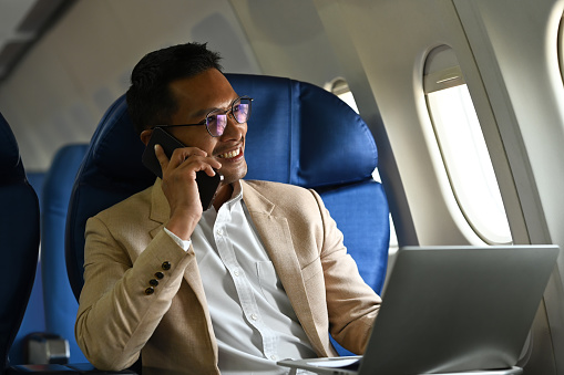 Successful businessman passenger talking on mobile phone while sitting in airplane cabin near windows.