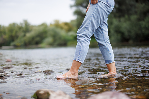 Close-up shot of female legs in jeans crossing river on sunny day