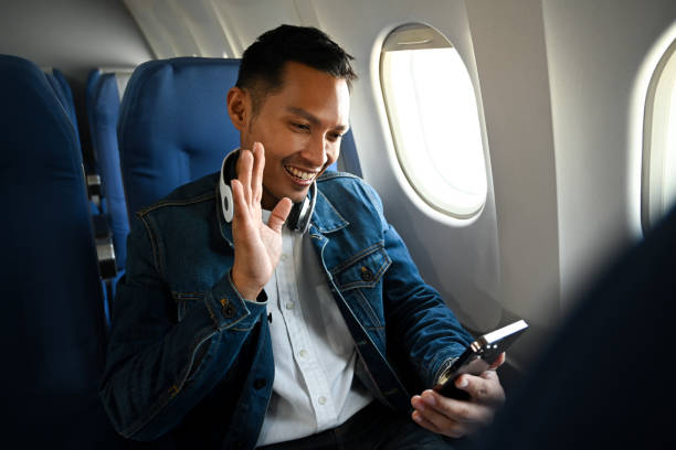 istock Smiling young hipster male passengers using smart phone having video call on mobile phone while sitting on aircraft cabin. 1459547391